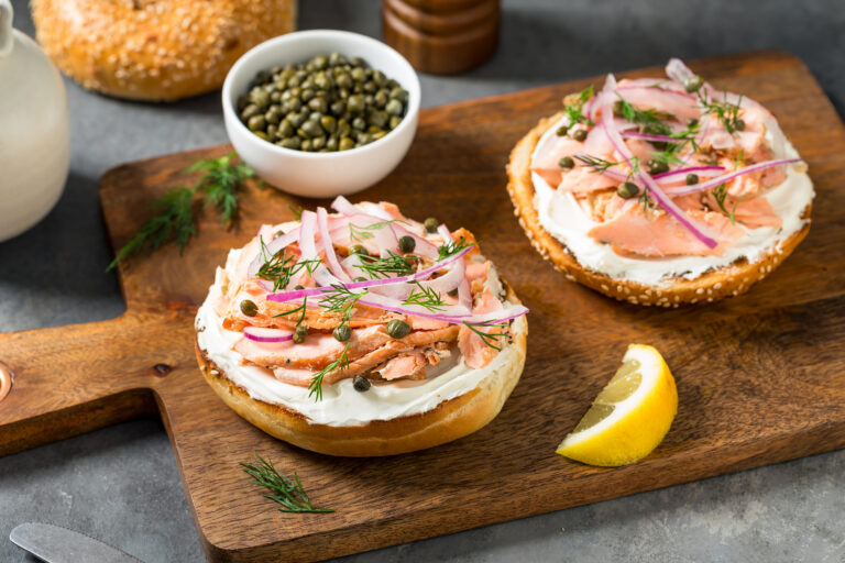 Open bagels with cream cheese, smoked fish, red onion and capers on a board