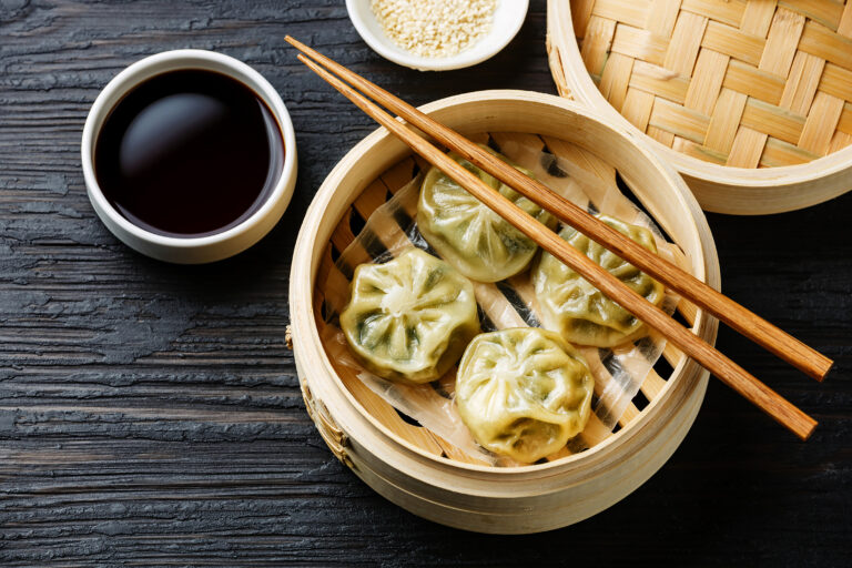 Steamed dumplings in a bamboo basket with a dish of soy dipping sauce