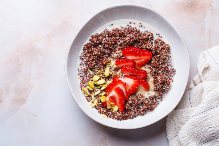 A breakfast bowl of red quinoa with sliced strawberries and pistachios