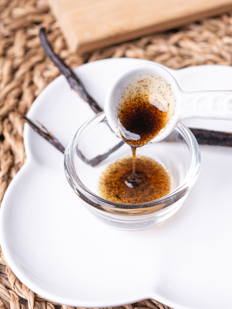 Vanilla bean paste spooned from a glass dish, with whole vanilla pods