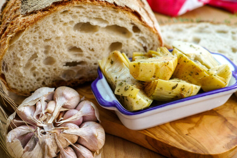Marinated artichoke hearts in a dish with crusty Italian bread and garlic