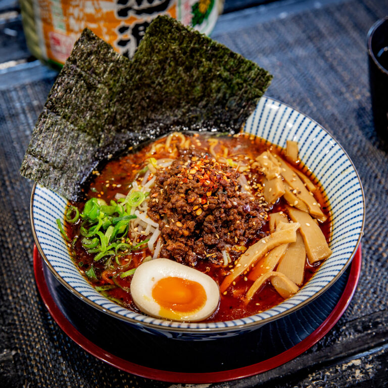 A bowl of spicy Sichuan pork ramen with sliced bamboo shoots and a soft egg